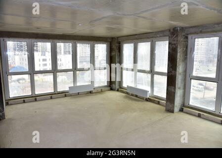 Intérieur inachevé de l'appartement en construction avec mur en béton gris et fenêtres à double vitrage dans un immeuble résidentiel de plusieurs étages à un inconvénients Banque D'Images