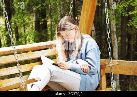 Une adolescente lit un livre tout en étant assise sur une balançoire Banque D'Images