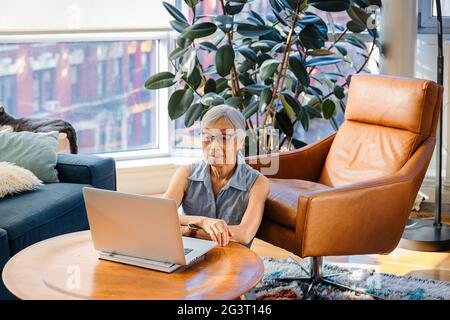 Femme asiatique senior assise et utilisant un ordinateur portable à la maison dans le salon Banque D'Images
