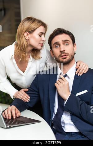 Séduction dans le concept de bureau. Jolie femme touchant un collègue masculin, qui s'assoit à la table, regardant la caméra mal penchée et touche son Banque D'Images