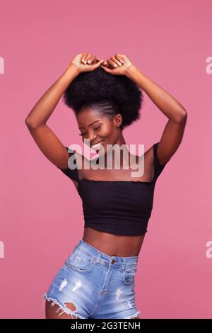 Magnifique jeune fille afro-américaine avec des cheveux afro posant avec les bras levés vêtu d'un haut noir et jeans en denim sur la tige sale Banque D'Images