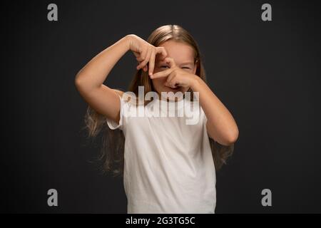 Amour geste heureuse fille de 8,10 ans tenant ses mains ensemble faisant une forme de coeur et regardant à travers elle portant t-shirt blanc Banque D'Images