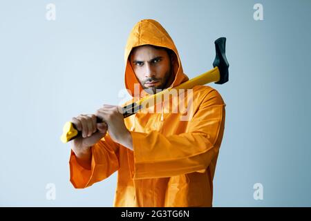 Jeune homme sérieux en imperméable brillant tenant une grosse hache sur son épaule Banque D'Images