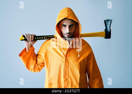 Jeune homme sérieux en imperméable brillant tenant une grosse hache sur son épaule Banque D'Images