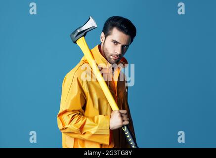 Jeune homme sérieux en imperméable brillant tenant une grosse hache sur son épaule Banque D'Images