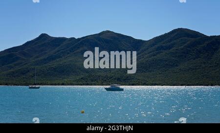 un bateau à moteur et un yacht amarrés au large de la côte sur une mer calme, avec une lumière matinale sur fond de montagne Banque D'Images