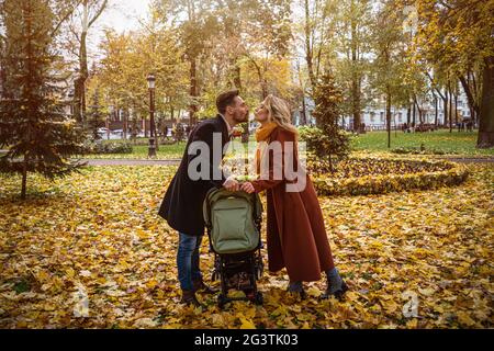 Famille marchant dans un parc d'automne avec un nouveau-né dans une poussette. Famille à l'extérieur dans un parc d'automne doré. Image teintée Banque D'Images