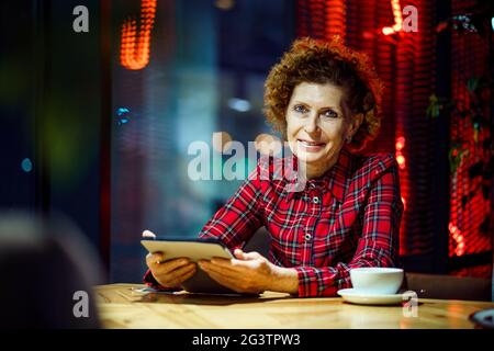 Femme âgée utilisant une tablette dans un café. Femme d'âge mûr se détendant dans un restaurant avec un Tablet pc. Les femmes âgées utilisent une tablette numérique à Banque D'Images