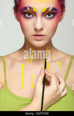 Portrait de femme avec maquillage d'art du visage et du corps inhabituel. La femme se peint avec une brosse. Banque D'Images