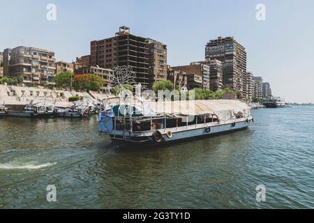 Un bateau avec des touristes sur une promenade sur le fleuve navigue le long du Nil dans le centre du Caire parmi les gratte-ciel et les attractions. Banque D'Images