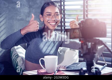 Jeune femme souriante vlogger montrant les pouces vers le haut tout en enregistrant son blog vidéo quotidien Banque D'Images