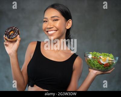 Portrait d'une belle jeune femme souriante avec un beignet et une salade saine Banque D'Images