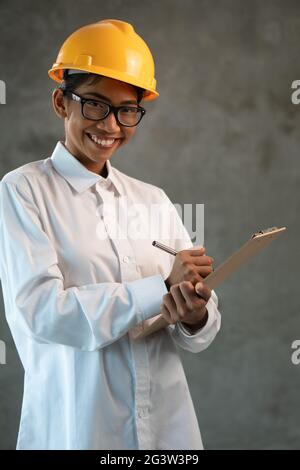 Portrait d'une femme asiatique souriante avec un presse-papiers sur un mur en béton Banque D'Images