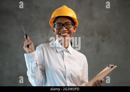 Portrait d'une femme asiatique souriante avec un presse-papiers sur un mur en béton Banque D'Images