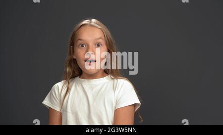 Très surpris, dumbfted petite fille regardant l'appareil photo portant t-shirt blanc et pantalon noir isolé sur fond noir Banque D'Images