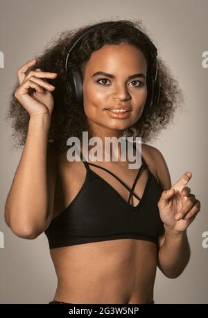 Dansant dans le casque jeune fille afro-américaine écoutant de la musique en portant le dessus noir et faire des mouvements de salsa avec les mains dans l'air, Banque D'Images