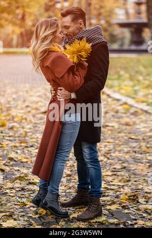 Embrasser un jeune couple. Un mari et une femme ont embrassé le sourire en regardant les uns les autres dans le parc d'automne. Photo d'un jeune couple en plein air Banque D'Images