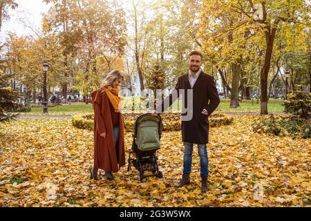 Marche dans un parc d'automne jeune famille avec un nouveau-né dans une poussette. Famille à l'extérieur dans un parc d'automne doré. Image teintée Banque D'Images