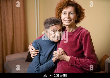 Vieille femme mignonne avec la maladie d'Alzheimer très heureuse et souriante quand la fille aînée prend soin d'elle, à la maison sur un canapé. Banque D'Images