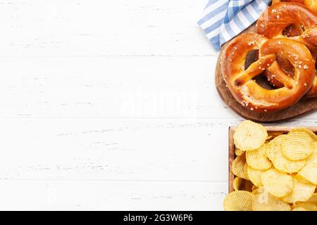 Bretzel maison fraîchement cuit avec sel de mer et chips de pommes de terre sur une table en bois. Collation classique à la bière. Vue de dessus du plan de travail avec espace de copie Banque D'Images