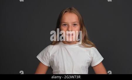 Petite fille stupéfait debout regardant heureux surpris à l'appareil photo portant un t-shirt blanc isolé sur gris foncé ou noir backgroun Banque D'Images