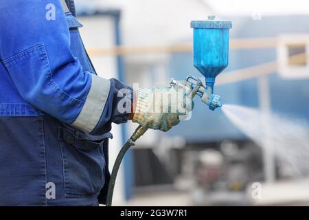 Vaporiser le pistolet à la main. Un ouvrier en combinaison et un gant tient un compresseur de pulvérisation pour peindre dans sa main. Banque D'Images