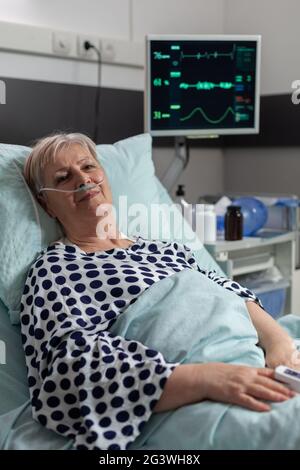 Patiente sénior se trouvant dans le lit d'hôpital après un traitement de récupération, recevant un médicament par voie intraveineuse. Oxymètre fixé au doigt pour surveiller la saturation en oxygène du sang. Banque D'Images