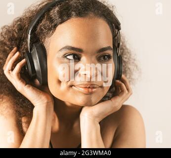 Jeune fille afro-américaine écoutant de la musique dans un casque portant un haut noir isolé sur fond gris, bouger émotionnellement. Conce Banque D'Images