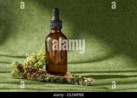 Bouteille en verre ambré avec sérum, huile essentielle, produit de beauté cosmétique anti-âge de collagène parmi la toile de fond vert mossy. Banque D'Images