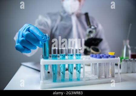 Gros plan des scientifiques mains dans des gants en latex bleu examine des échantillons de liquide chimique dans des tubes à essai en laboratoire scientifique. Recherche a Banque D'Images