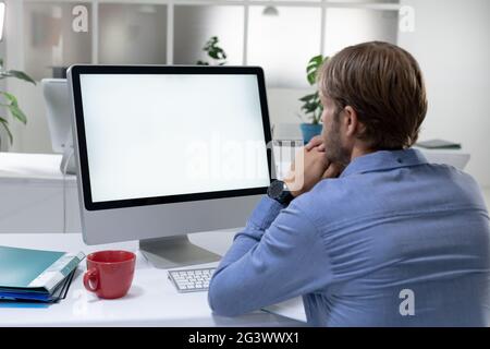 Vue arrière de l'homme d'affaires caucasien assis sur le bureau et vidéo appeler à l'aide d'un ordinateur de bureau Banque D'Images