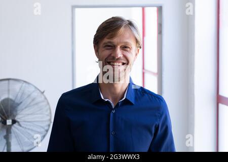 Portrait d'un homme caucasien souriant debout devant la fenêtre dans la salle blanche Banque D'Images