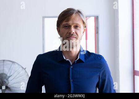 Portrait d'un homme caucasien souriant debout devant la fenêtre dans la salle blanche Banque D'Images