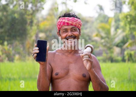 Rural Indien Homme montrant sur téléphone mobile dans le domaine agricole Banque D'Images