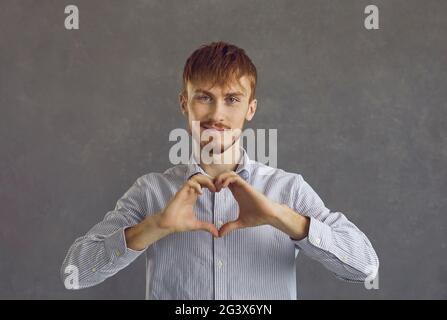Homme caucasien à poil rouge faisant un geste de coeur montrant l'amour et la charité Banque D'Images