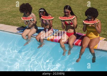 Divers groupes d'amis qui mangent de la pastèque au bord de la piscine Banque D'Images