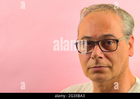 gros plan gris cheveux homme regardant droit devant sur un fond rose Banque D'Images