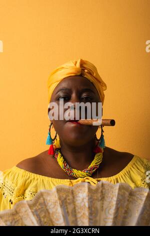 portrait d'une femme afro-américaine sérieuse d'âge moyen fumant un cigare sur du jaune Banque D'Images