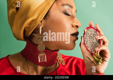 jeune afro-américaine avec des yeux fermés tenant une moitié de coupe de fruit de dragon sur le vert Banque D'Images