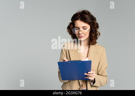 femme d'affaires en lunettes et blazer tenant le presse-papiers isolé sur gris Banque D'Images