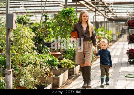 Femme avec une plante en pot et son fils marchent dans la serre Banque D'Images