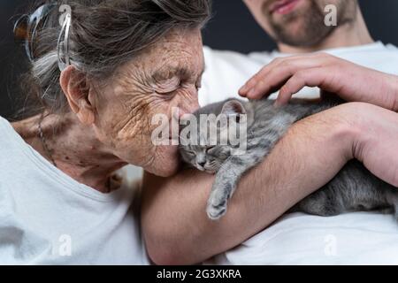 Bonne femme âgée qui se câlin et embrasse, se blottir pour faire face à un petit chaton gris mignon, qui a tenu dans les bras par son petit-fils pendant la visite Banque D'Images