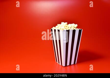 Pop-corn dans un emballage en carton coloré. Tas de pop-corn salé dans du potter à rayures sur fond rouge. Banque D'Images