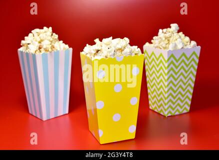 Pop-corn dans un emballage en carton coloré. Tas de pop-corn salé dans du potter à rayures sur fond rouge. Banque D'Images