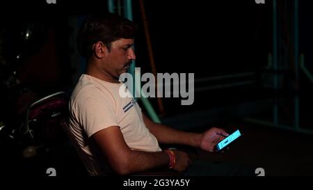 Indien mûr gars utilisant le téléphone mobile regarder des vidéos youtube. Homme asiatique décontracté et assis sur un canapé en plein air. Banque D'Images