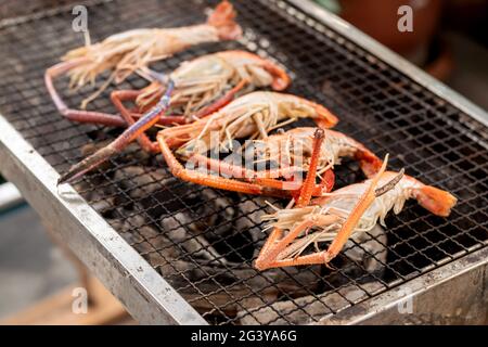 Gros plan quelques crevettes de rivière grillées sur le porte-fer au-dessus du charbon de bois. Banque D'Images