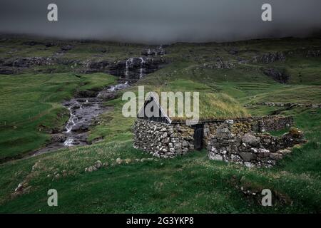 Huttes avec un toit en herbe et une chute d'eau dans le village de Saksun sur l'île de Streymoy, îles Féroé Banque D'Images