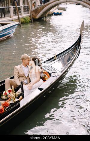 Mariage en Italie à Venise. La mariée et le marié se promettent dans une gondole classique en bois le long d'un étroit canal vénitien. Gros plan des câlins Banque D'Images