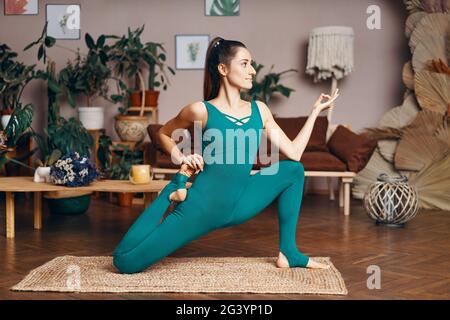 Jeune femme sportive pratiquant le yoga à la maison faisant Eka Pada Rajakapotasana, une variante de pigeon à une jambe Banque D'Images