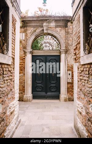 Gros plans des façades de bâtiments à Venise, Italie. Double porte bleue en bois, de type voûté, avec une arche métallique forgée au-dessus de la porte, a Banque D'Images